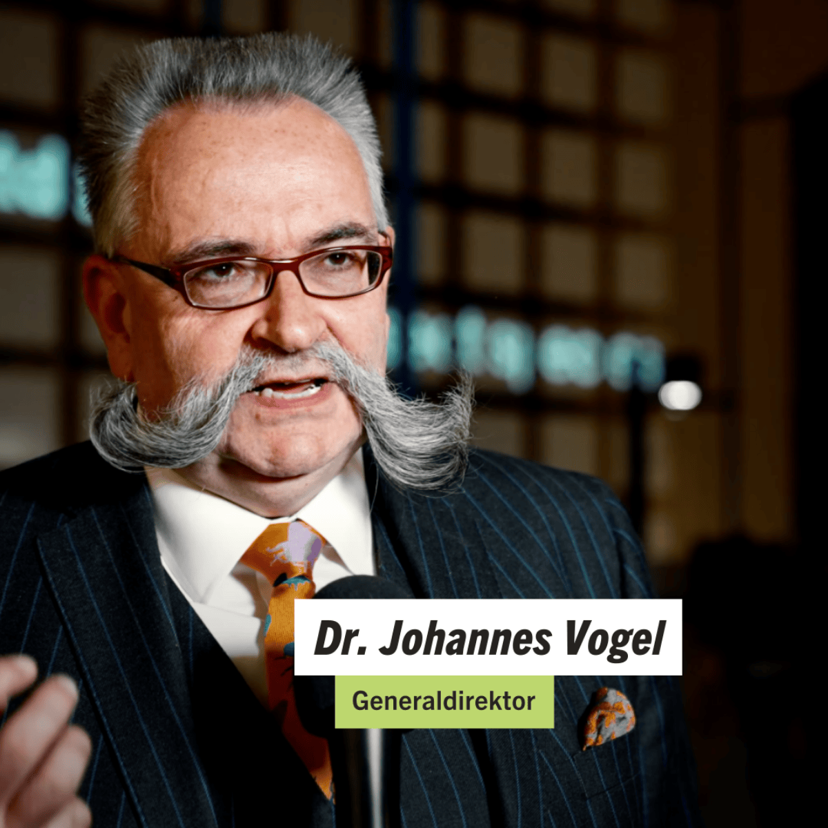 Interview-Thumbnail mit einer Person und eingeblendeter Namenszeile vor Museumsregalen