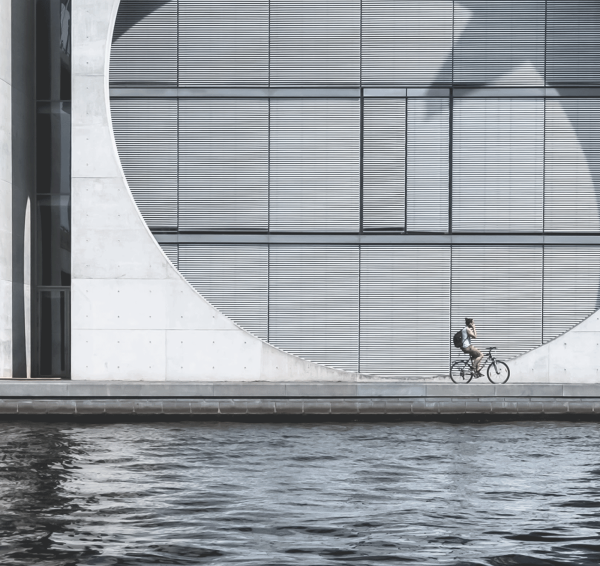 Ein Teil des Bundeskanzleramts in Berlin ist zu sehen. Vorne sieht man die Spree, am Ufer f&auml;hrt ein Fahrradfahrer.