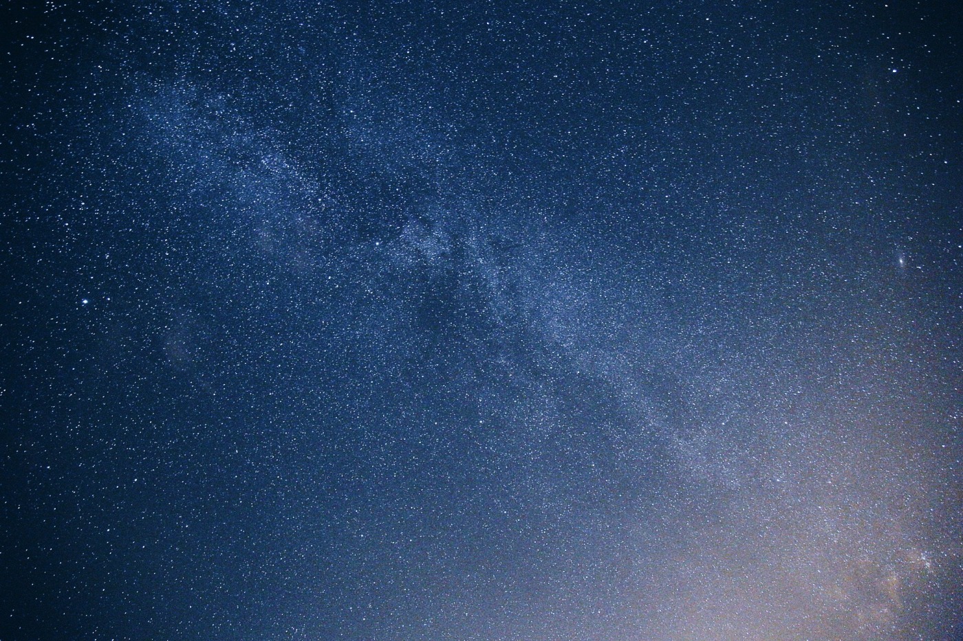 Blick in den Sternenhimmel auf die Milchstra&szlig;e bei Nacht. Von der rechten unteren Ecke kommt ein leichter Lichtschein.